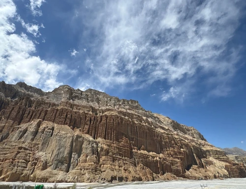 Dramatic eroded cliffs and rugged rock formations in Lo Manthang, Upper Mustang, Nepal, beneath a blue sky with scattered clouds.