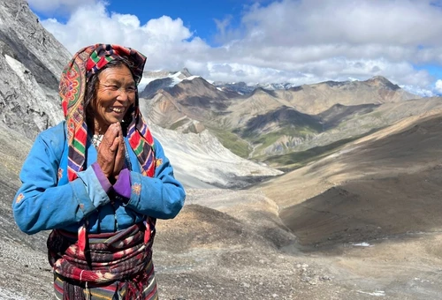 Local woman in traditional Tibetan dress standing in the rugged mountain landscape of the Dolpo Region in Nepal.