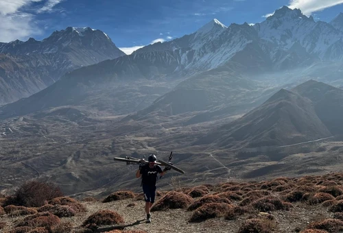 Trekker carrying gear walking through high altitude mountain landscape in Tibet with snow-covered peaks