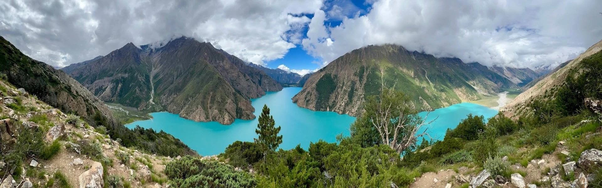 Panoramic view of turquoise Phoksundo Lake surrounded by dramatic Himalayan mountains and green valleys in the Dolpo Region of Nepal.