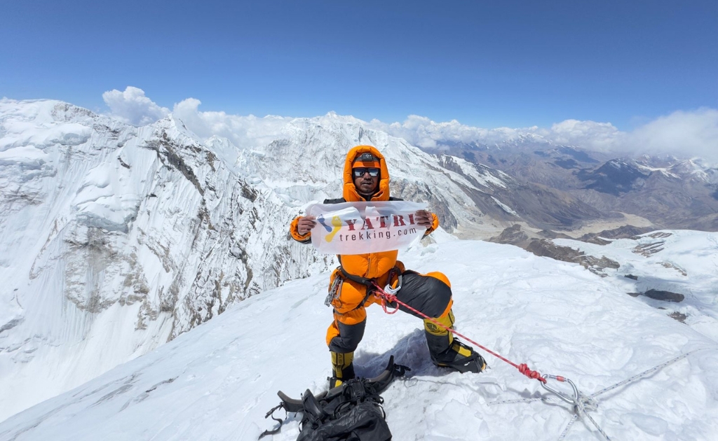 Climber at Himlung Himal summit holding Yatri Trekking banner with panoramic Himalayan mountain views in Nepal