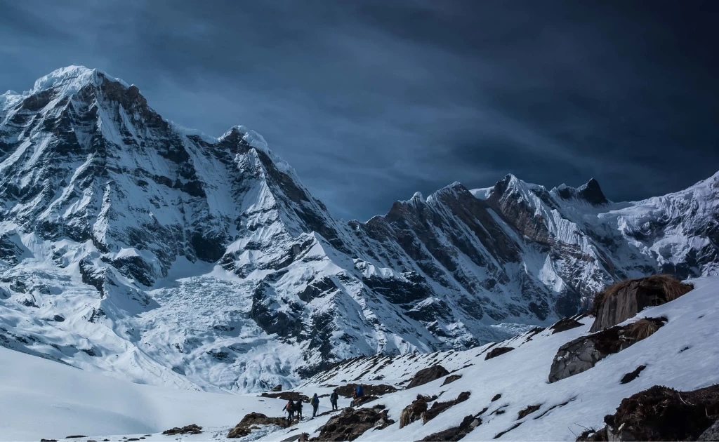 Mount Annapurna I peak with trekkers walking across a snowy trail and glacier in the foreground