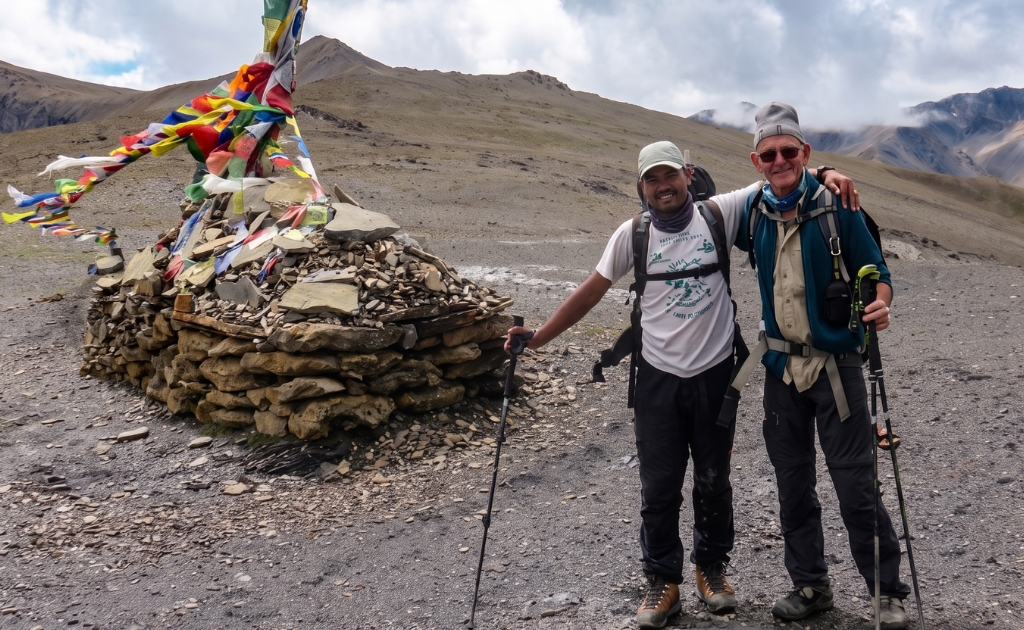 Trekkers standing at Kang La Pass in Upper Dolpo surrounded by barren Himalayan landscapes, prayer flags, and dramatic mountain scenery.