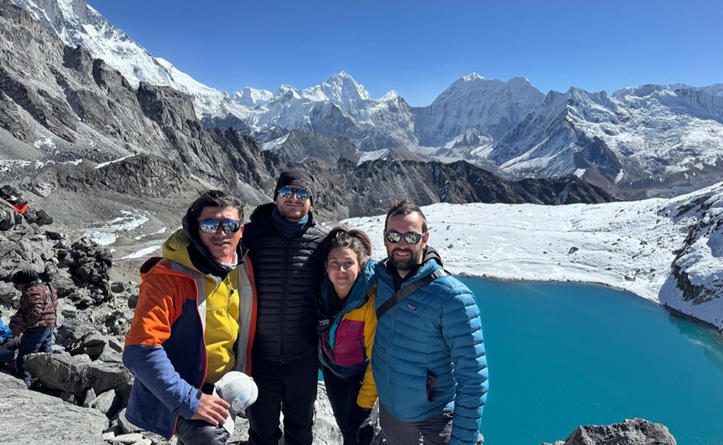Trekkers walking beside the turquoise Gokyo Lakes with snow-covered Himalayan peaks in the background.