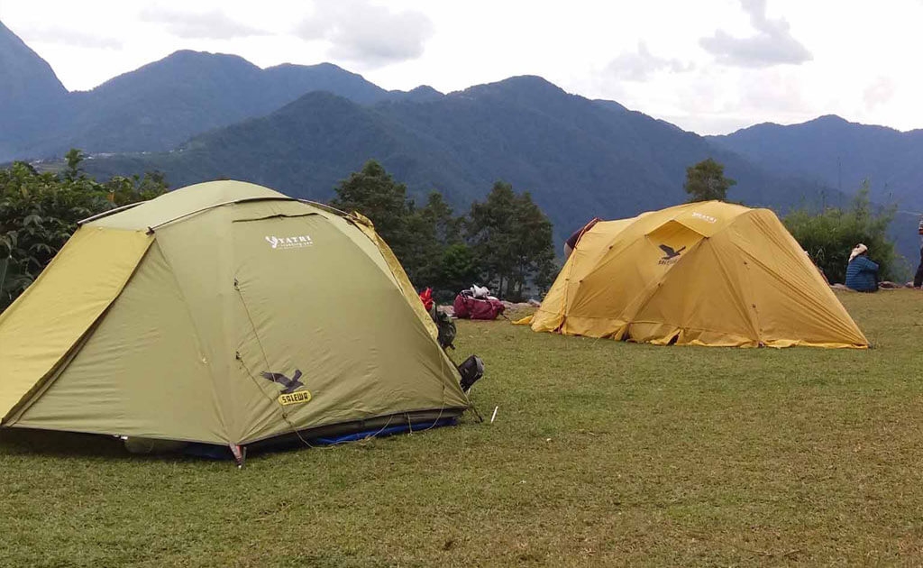 Camping tents on grassy trail during monsoon season in the Kanchenjunga region with cloudy Himalayan hills in eastern Nepal
