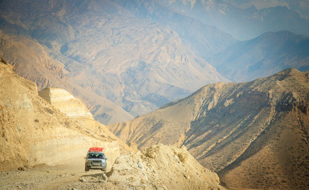 4WD jeep traveling along a remote mountain road in Upper Mustang, Nepal, surrounded by dramatic Himalayan desert landscapes and rugged valleys.