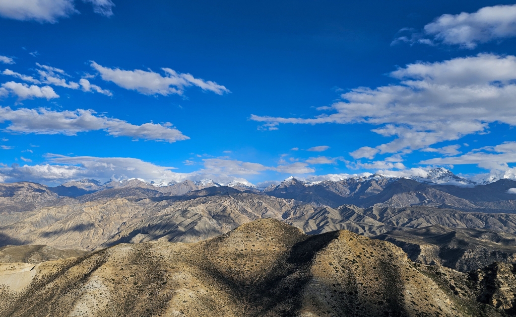 Panoramic view of the rugged Himalayan desert landscape on the trekking route to Lo Manthang in Upper Mustang, Nepal, with snow-capped peaks in the distance.