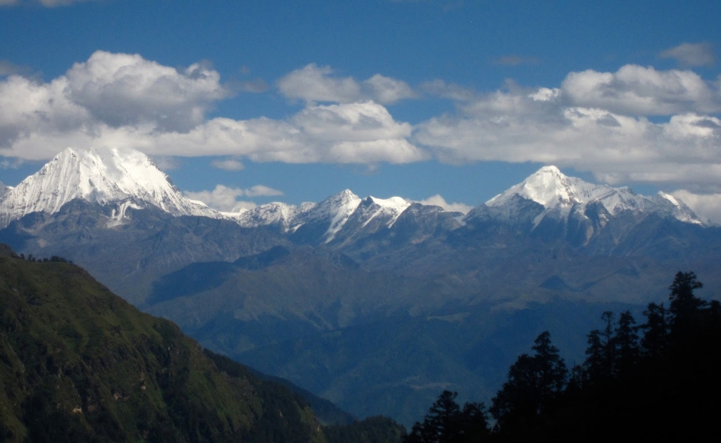 Panoramic view of beautiful snow-capped mountains and green hills in Mugu District under a bright blue sky with scattered clouds in Nepal