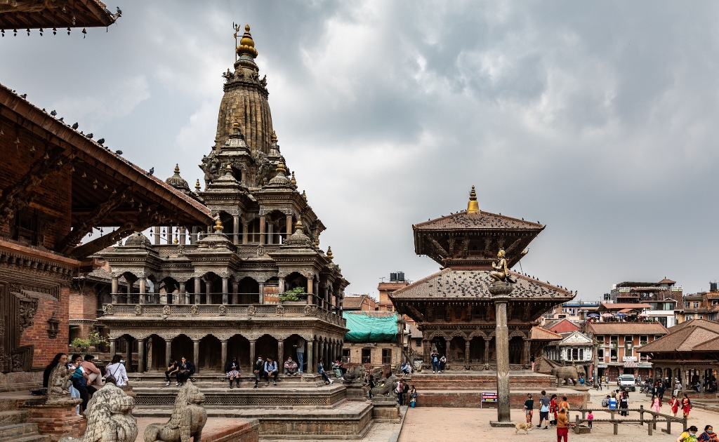 Patan Durbar Square in Lalitpur, Nepal, featuring the stone Krishna Temple, traditional Newari pagoda temples, and historic palace courtyards under a dramatic sky.